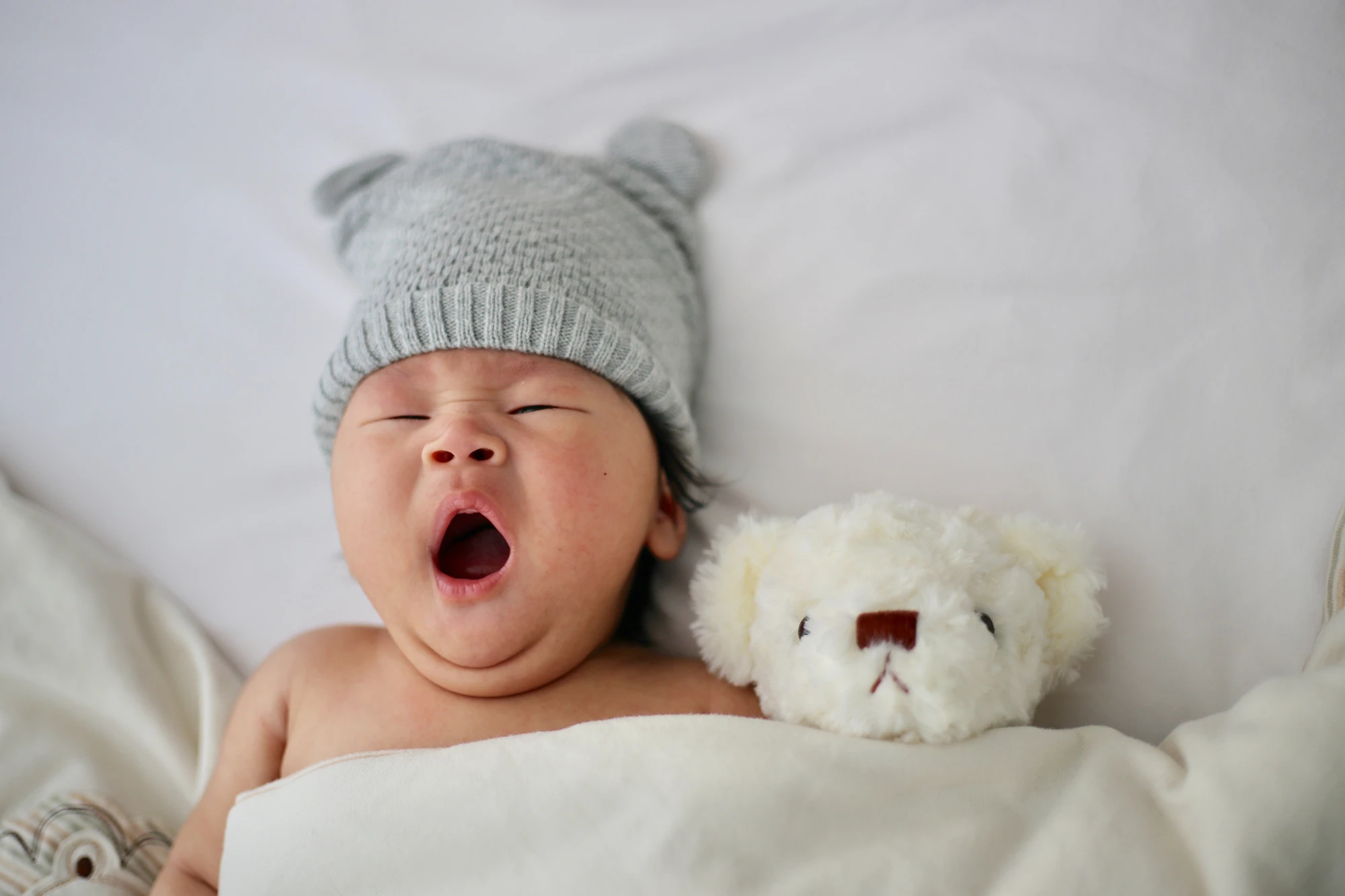 un bébé qui baille dans un lit avec son doudou